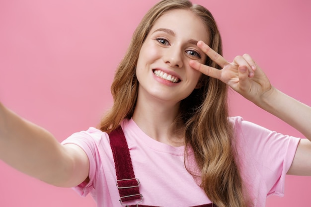 Körperpositiv, Narben und Hautpositivitätskonzept. Porträt eines charmanten, sorglosen jungen Mädchens mit Wunde am Arm, das die Hände in Richtung der Kamera zieht und Selfie macht, um ein Friedenszeichen mit breitem Lächeln zu machen.