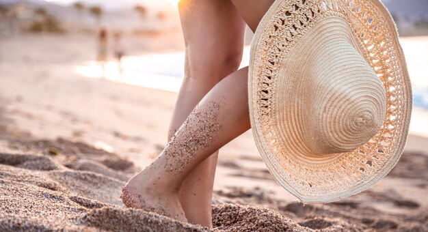 Körperteil. Füße einer Frau, die am Strand bei Sonnenuntergang mit einem Hut steht.