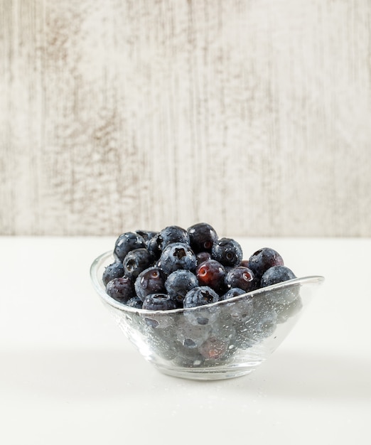 Köstliche Blaubeeren in einer Glasschale auf einer weißen und grungy grauen Wand. Seitenansicht.