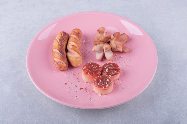 Köstliche Bratwürste mit Ketchup auf rosa Teller.