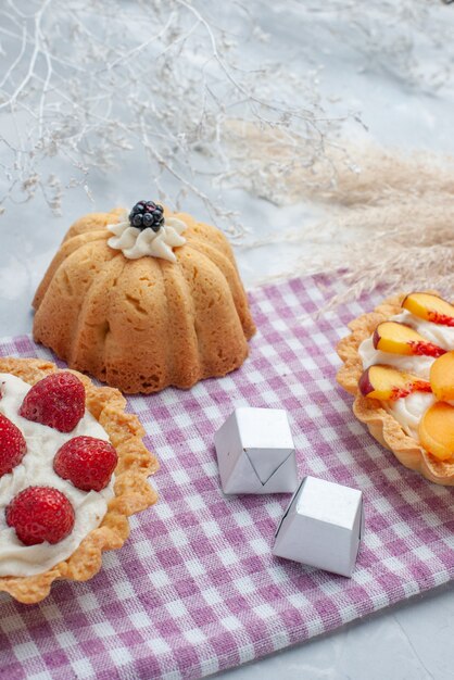 köstliche cremige Kuchen mit geschnittenen Früchten zusammen mit Pralinen und Tee auf hellem Schreibtisch, Kuchenkeks süße Sahne backen Tee