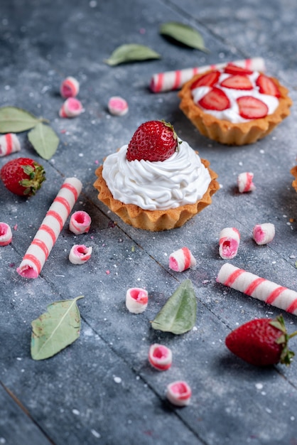 köstliche cremige Kuchen mit geschnittenen und frischen Erdbeeren zusammen mit Stockbonbons auf grauer, süß gebackener Beere mit Obstkuchen