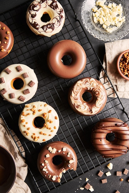 Köstliche Donuts bedeckt mit der weißen und braunen Schokoladenglasur mit den Zutaten auf einem Tisch