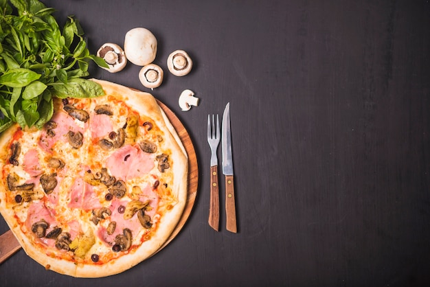 Köstliche Fleisch- und Pilzpizza mit Gabel und Messer auf dunklem Hintergrund