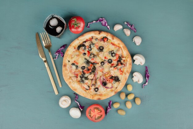 Köstliche heiße Pizza mit Oliven, Pilzen und Tomaten auf blauer Oberfläche.