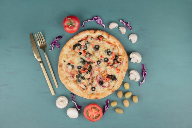 Köstliche heiße Pizza mit Oliven, Pilzen und Tomaten auf blauer Oberfläche.