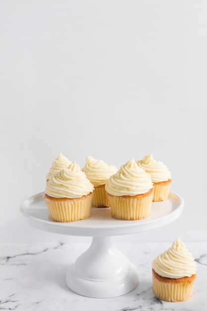 Köstliche kleine Kuchen auf Kuchen stehen über Marmortabelle gegen weißen Hintergrund