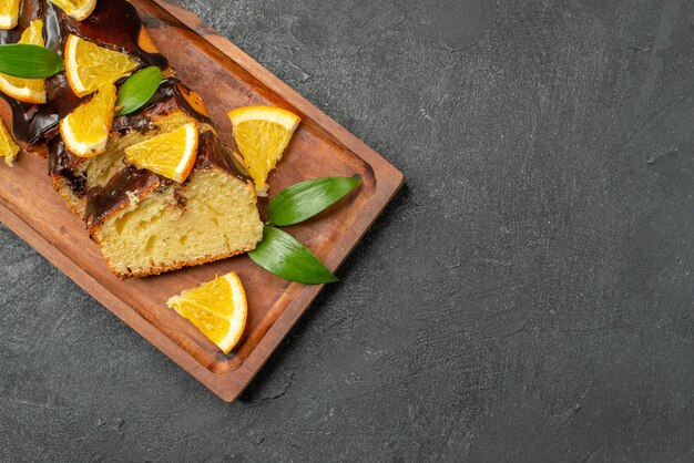 Köstliche Kuchen verziert mit Orange und Schokolade auf hölzernem Schneidebrett auf schwarzem Tisch