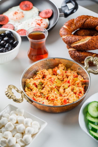 Köstliche Mahlzeiten in einer Pfanne und einem Topf mit Salat, Gurken, türkischem Bagel, einer Tasse Tee mit hohem Blickwinkel auf eine weiße Oberfläche