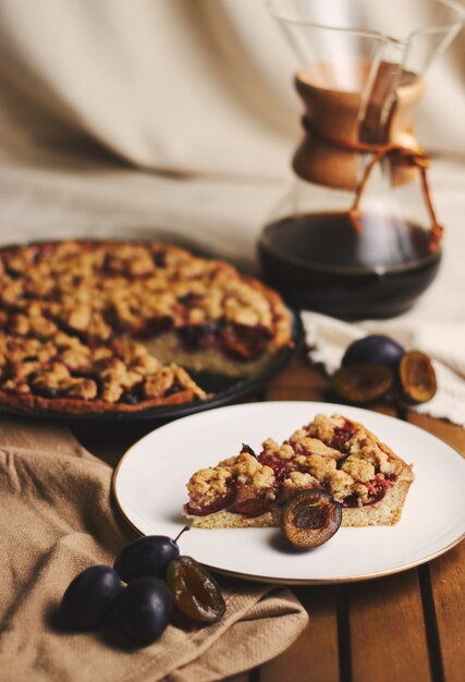 Köstliche Pflaumenpastete mit Chemex-Kaffee und Zutaten mit Stoff auf einem Holztisch mit Stoff