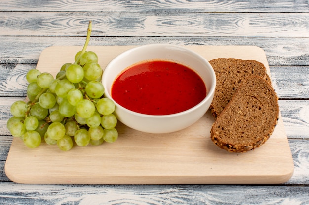 köstliche Tomatensuppe mit Brotlaib und grünen Trauben auf grauem Suppenessen