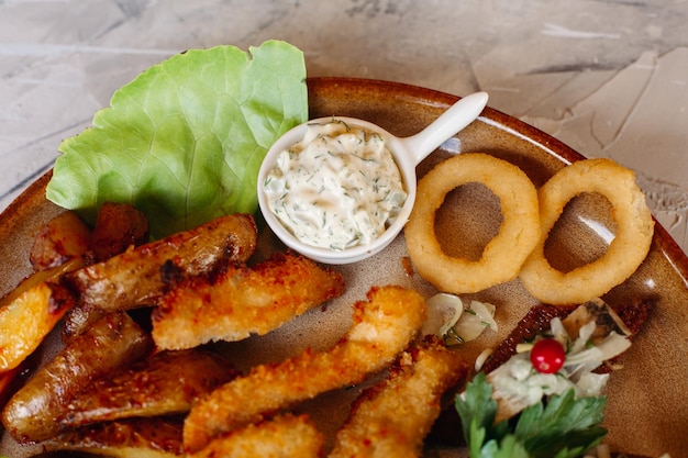 Köstliche Vorspeisen für Bier und leichte alkoholische Getränke, die auf einer mit Salatblättern und Käse dekorierten Tonplatte liegen, knusprige Hühnchen-Nuggets-Kanapees mit Hering und Kirschtomaten-Knoblauchsoße