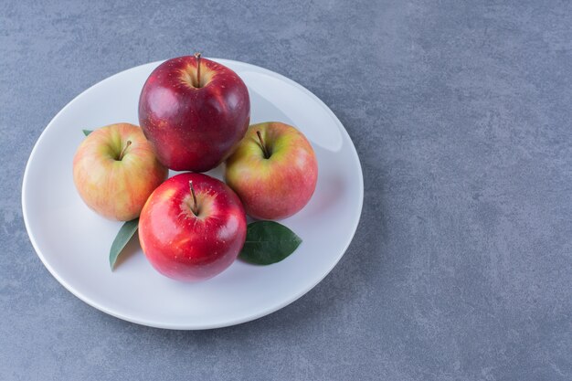 Köstlicher Apfel mit Blättern auf Teller auf der dunklen Oberfläche