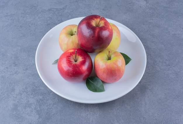 Köstlicher Apfel mit Blättern auf Teller auf Marmortisch.