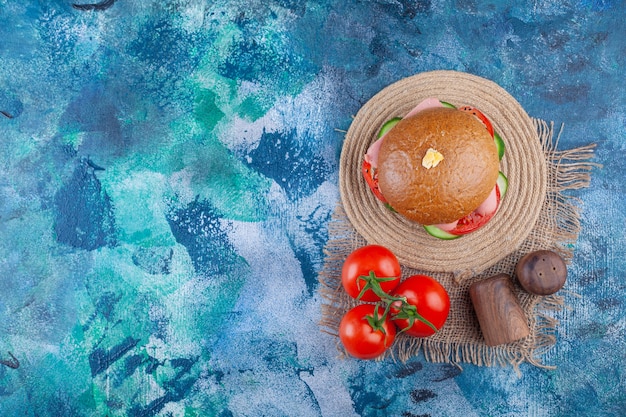 Köstlicher hausgemachter Burger mit frischen Tomaten auf blauer Oberfläche.