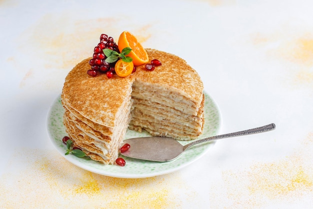 Köstlicher hausgemachter Crêpe-Kuchen, dekoriert mit Granatapfelkernen und Mandarinen.