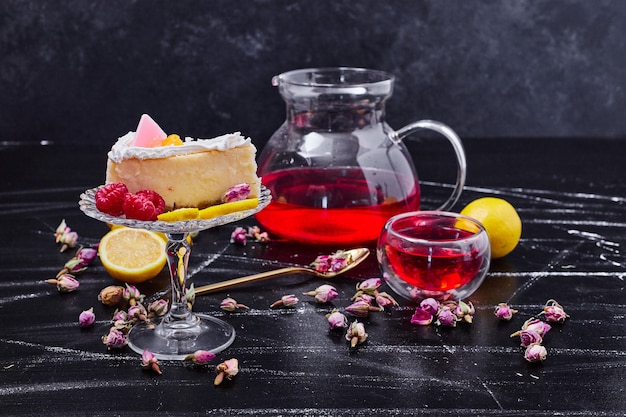 Köstlicher Käsekuchen auf Glastortenplatte neben Teekanne mit getrockneten Blumen.