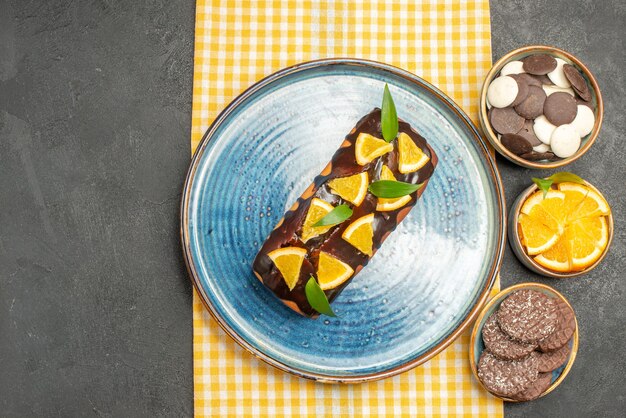 Köstlicher Kuchen, dekoriert mit Orange und Schokolade auf gelb gestreiftem Handtuch und Keksen