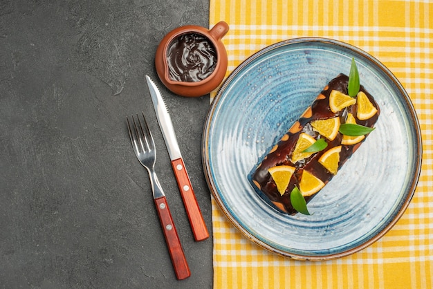 Kostenloses Foto köstlicher kuchen, dekoriert mit orange und schokolade, serviert mit gabel und messer auf dunklem tisch