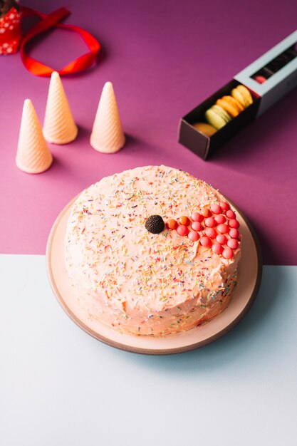 Köstlicher Kuchen mit Waffelkegeln und -makronen auf rosa und weißem Hintergrund