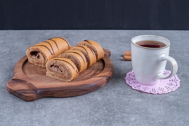 Köstlicher Rollkuchen auf Holzplatte mit Tasse Tee