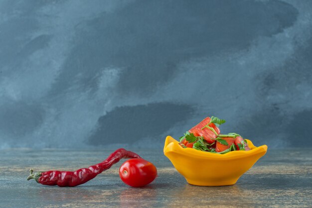 Köstlicher Salat im gelben Teller mit Pfeffer und Tomate auf Marmorhintergrund