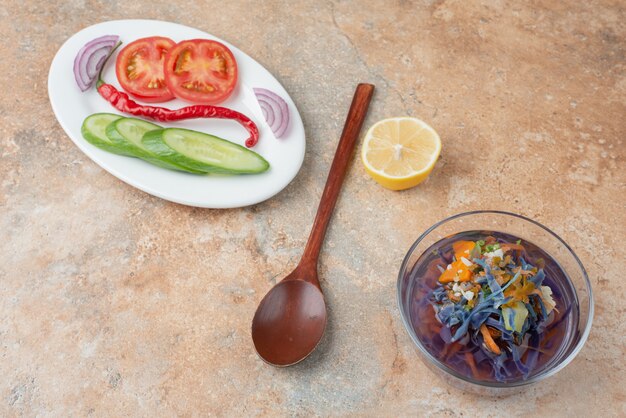 Köstlicher Tee mit Gurke, Tomate, Zitronenscheibe und Löffel auf weißem Teller