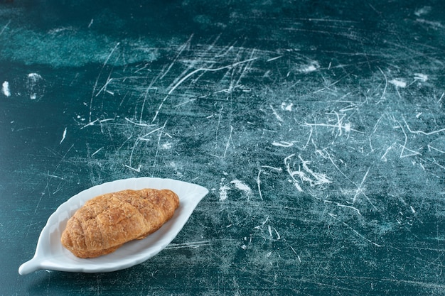 Köstliches Croissant auf einer Platte auf dem blauen Tisch.