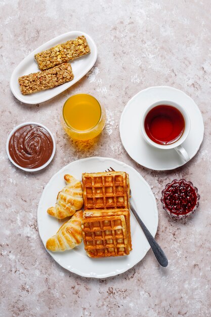 Köstliches Frühstück mit Kaffee, Orangensaft, Waffeln, Hörnchen, Stau, Nusspaste auf heller, Draufsicht