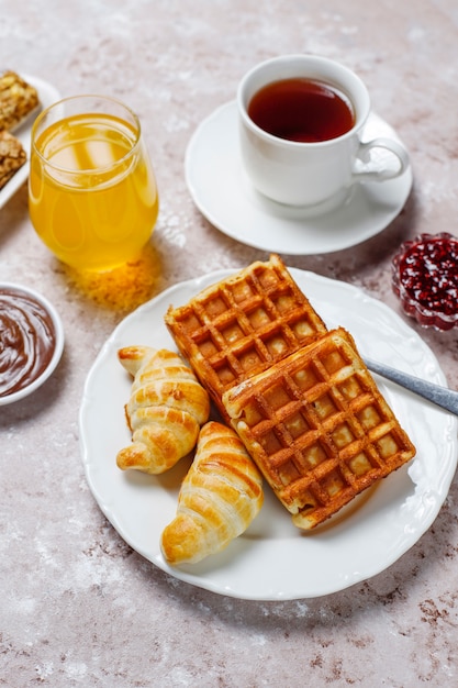 Köstliches Frühstück mit Kaffee, Orangensaft, Waffeln, Hörnchen, Stau, Nusspaste auf heller, Draufsicht