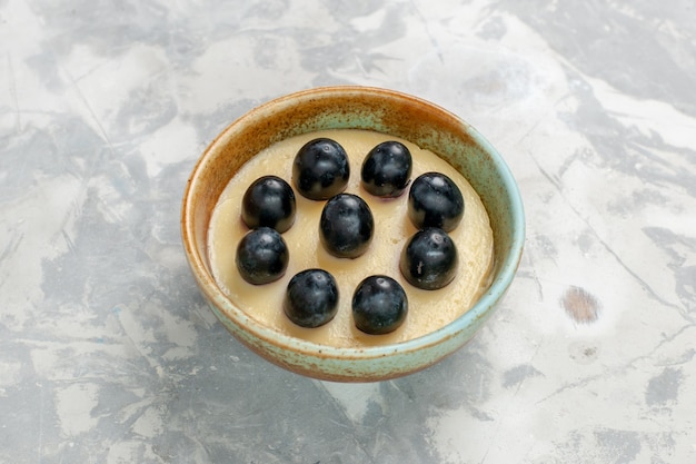 Köstliches Sahne-Dessert von vorne aus der Nähe mit Trauben oben in einem kleinen Topf auf weißer Oberfläche