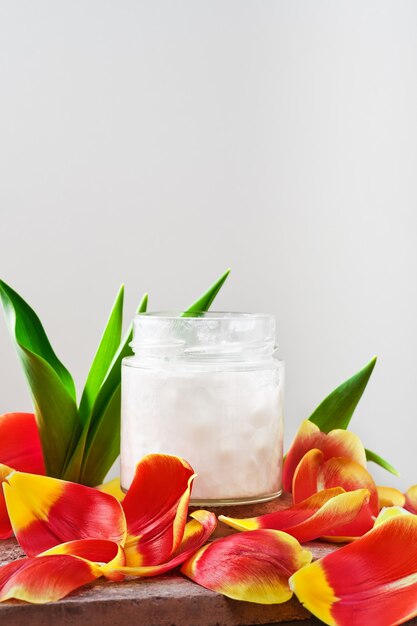Kokosöl in einem Glas auf Weiß, umgeben von Tulpenblättern, Nahaufnahme mit Kopierraum