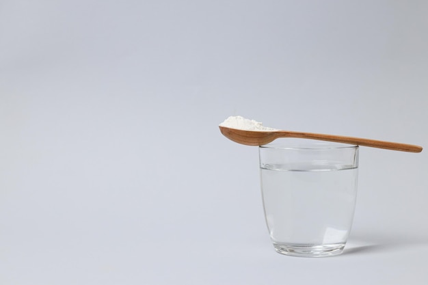 Kollagenpulver in einem Holzlöffel mit einem Glas Wasser