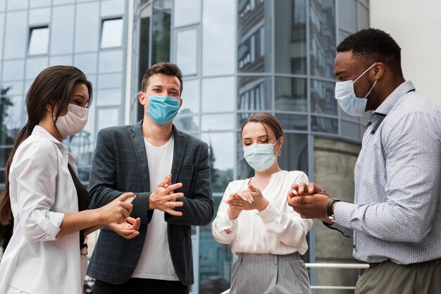 Kollegen desinfizieren Hände im Freien während einer Pandemie, während sie Masken tragen