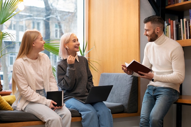 Kollegen, die in einer Bibliothek lernen, während sie einen Laptop und Notebooks verwenden