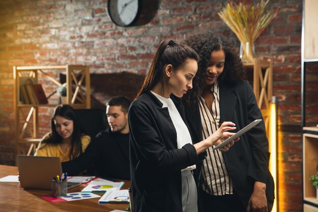 Kollegen, die in modernen Büros mit Geräten und Gadgets während eines kreativen Meetings zusammenarbeiten