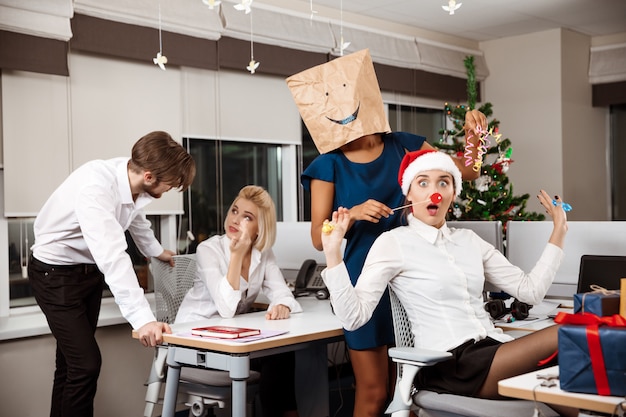 Kollegen feiern Weihnachtsfeier im Büro und trinken Champagner lächelnd.