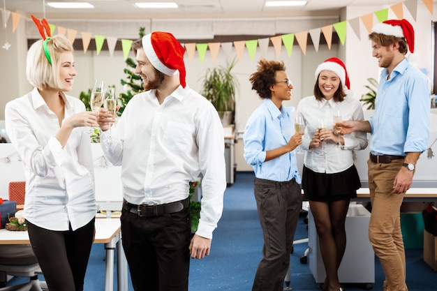 Kollegen feiern Weihnachtsfeier im Büro und trinken Champagner lächelnd.