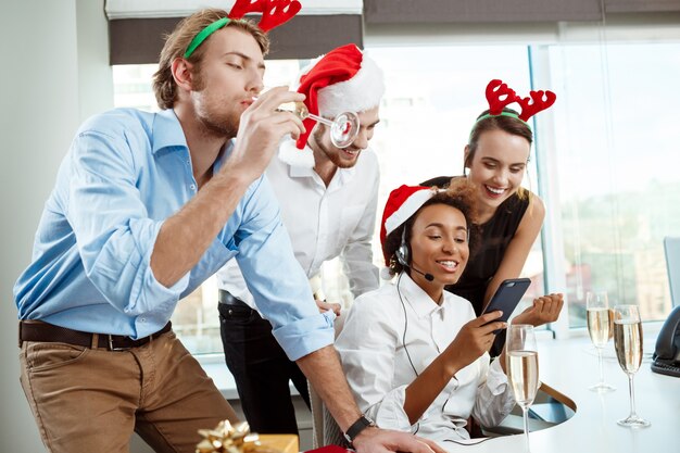 Kollegen feiern Weihnachtsfeier im Büro und trinken Champagner lächelnd.