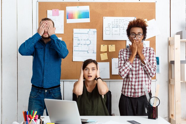 Kollegen schließen Mund, Augen und Ohren mit den Händen im Büro