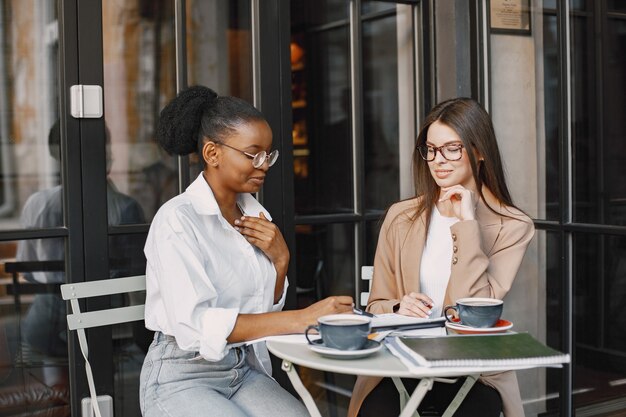 Kolleginnen diskutieren Daten im Café im Freien. Multirassische weibliche Personen, die die produktive Strategie für die Geschäftsprojektion mit Dokumenten im Straßencafé analysieren