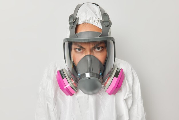 Ökologisches Problemkonzept Wütende unzufriedene Frau trägt Schutzanzug mit Kapuze und Atemschutzmasken, um zu verhindern, dass giftige Gase isoliert über grauem Hintergrund in die Luft gelangen, schützt die Natur