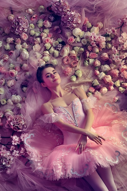 Komfortabel. Draufsicht der schönen jungen Frau im rosa Ballett-Tutu, umgeben von Blumen. Frühlingsstimmung und Zärtlichkeit im Korallenlicht.