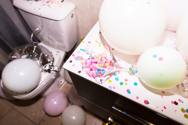 Konfetti, die vom Martinglas mit Ballonen auf Schreibtisch im Badezimmer fallen