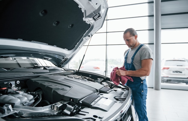 Konzentration bei der Arbeit. Mann in blauer Uniform arbeitet mit kaputtem Auto. Reparaturen durchführen