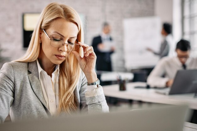 Konzentrierte Geschäftsfrau, die an ihrem Schreibtisch im Büro arbeitet. Es gibt Leute im Hintergrund