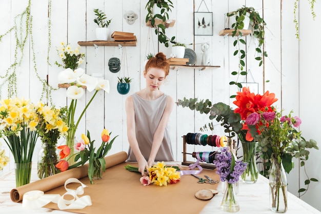 Konzentrierte junge Frau, die bunten Blumenstrauß in der Werkstatt sammelt