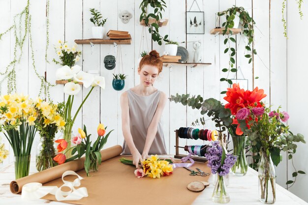 Konzentrierte junge Frau, die bunten Blumenstrauß in der Werkstatt sammelt