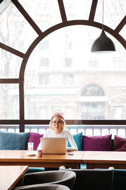 Konzentrierte junge frau, die mit laptop im café arbeitet