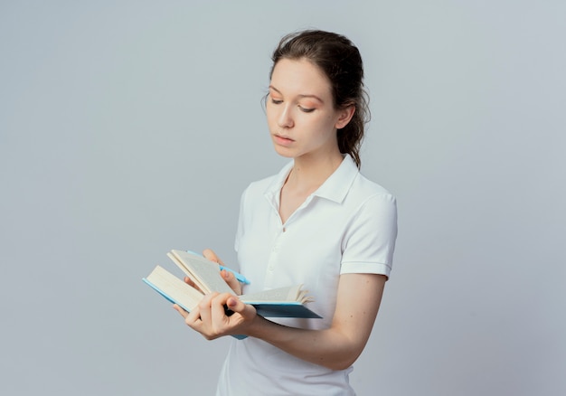 Konzentrierte junge hübsche Studentin, die Buch mit Stift in einer anderen Hand hält und liest, lokalisiert auf weißem Hintergrund mit Kopienraum